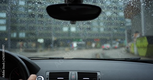 POV car driving on wet city street during rainy weather with raindrops on windshield