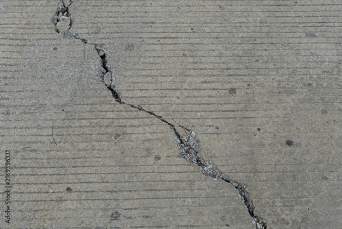 Photography Top-down close-up of a jagged diagonal crack running across a grooved concrete pavement in horizontal view
