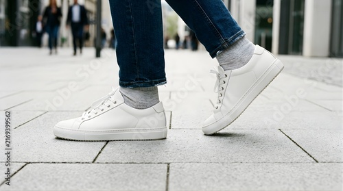 Person wearing white leather sneakers walking on a grey urban city street