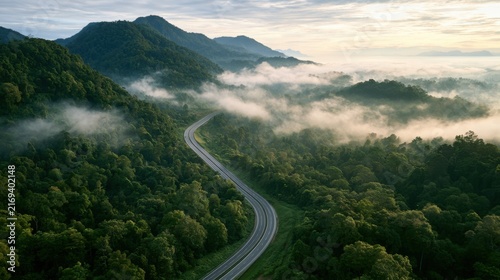 Aerial view of a winding highway cutting through lush tropical forest and mountain landscape under misty skies
