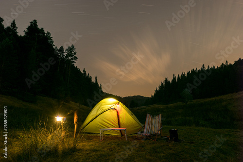 Cuadro en lienzo A bright yellow glowing tent set up at a night campsite surrounded by dark pine forest