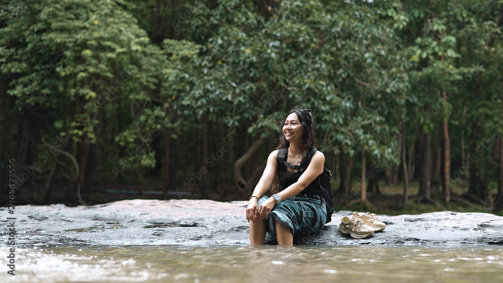Fototapeta premium Happy Woman Backpacker Relaxing with Feet in River Water Outdoors