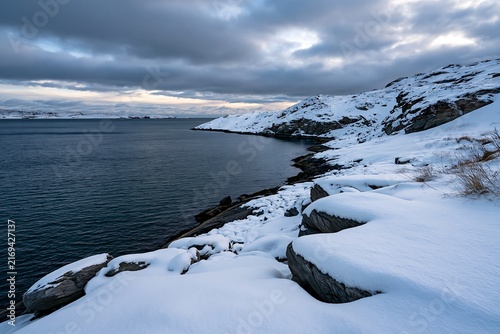 Winter landscape with snow covered rocks by the cold ocean water at dusk
