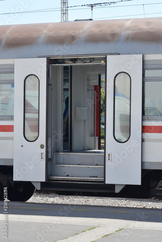 An open automatic sliding door entry of a modern passenger train car standing at a platform with visible stairs and interior details