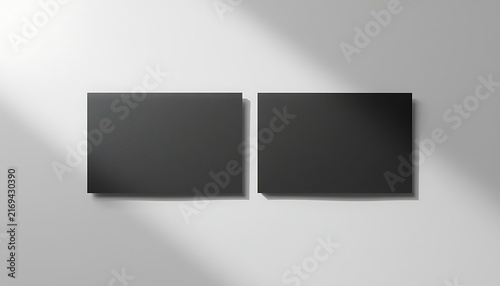Two blank black business cards mockup on white wall with soft sun shadow.
