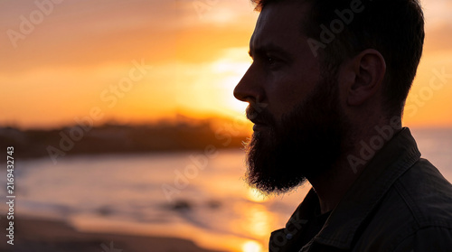 Bearded man enjoying the serene sunset by the ocean, a peaceful moment on beard day reflecting the beauty of nature and tranquil coastal vibes