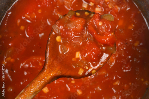 Foto Detailed close up view of a rich chunky tomato and roasted pepper sauce with garlic and onion chunks on a wooden spoon