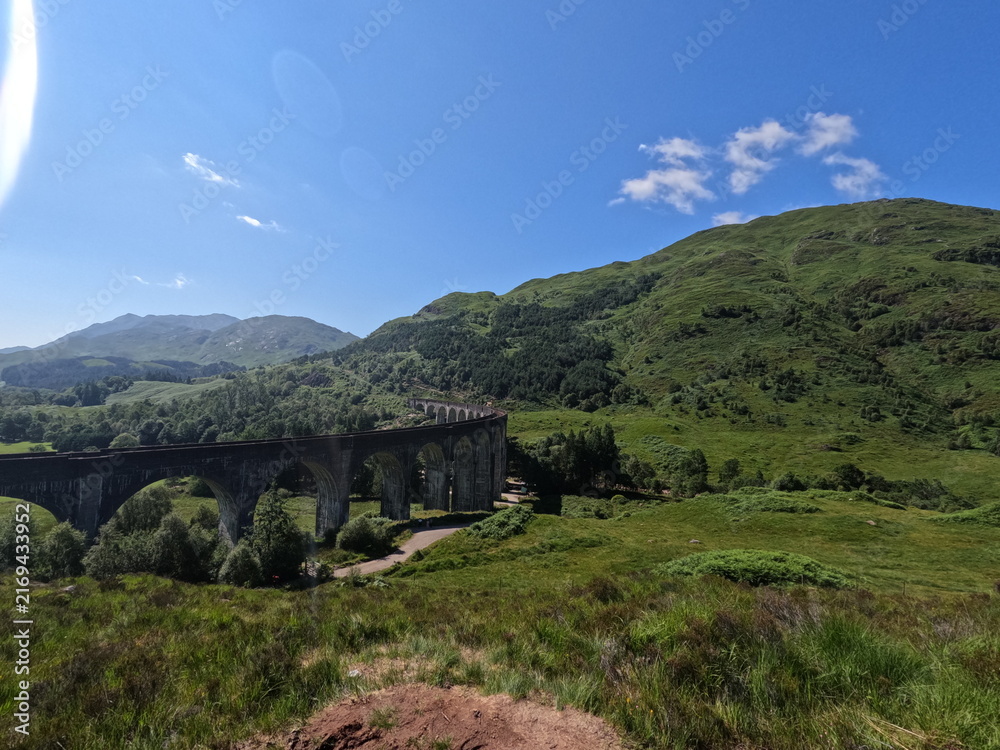 Fototapeta premium Historic Glenfinnan Viaduct curved concrete railway bridge in lush green mountains of Scottish Highlands, iconic Scotland landmark.