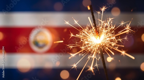 Sparkling firework stick macro photo with blurred Costa Rican national flag for independence day celebration