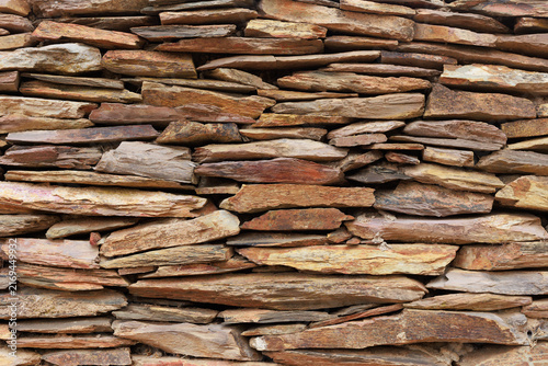 Close-up of a traditional dry stone wall built from irregular layers of natural stone. The weathered rocks display earthy shades of brown, beige, ochre and reddish tones, creating a detailed rustic