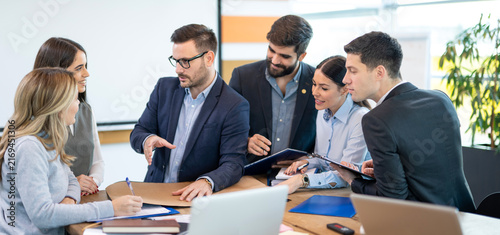 Manager explains ideas and guides a collaborative planning session while colleagues listen and take notes in a modern office.