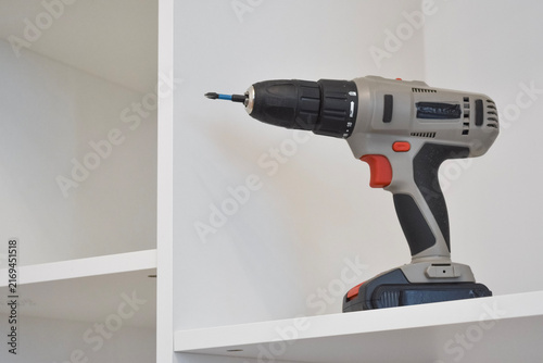 Obraz na plátne Close-up of a grey and red cordless drill resting on a shelf of a white modular