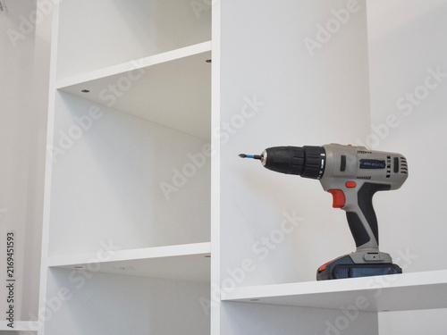 Bild auf Leinwand Close-up of a grey and red cordless drill resting on a shelf of a white modular