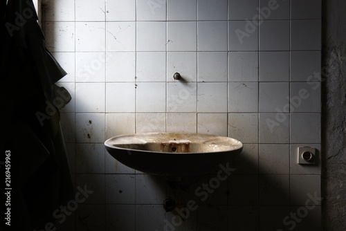 Dirty sink on wall covered with tiles in abandoned building