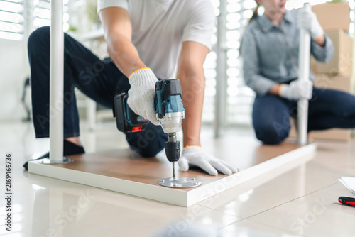 Young asian coworkers assembling office furniture together with power drill and hand tools during workplace relocation