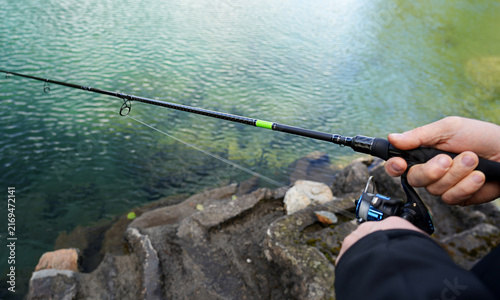 Konstfotografi Fishing rod held by a person with a black jacket, casting line into clear water