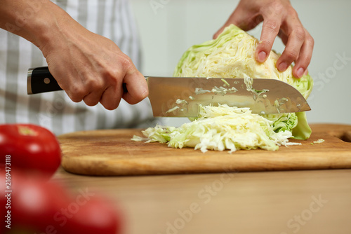 Person slicing fresh cabbage on wooden board preparing salad