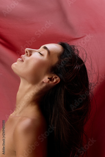 Sensual profile tilts upward beneath sweeping burgundy cloth and soft light. Concept of desire, self acceptance, perfume advertising and romantic expression.