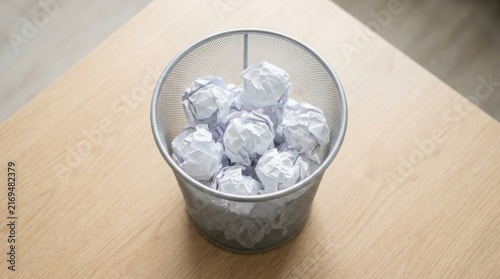 Metal mesh wastebasket full of crumpled paper balls on wooden desk, discarded ideas and creative failure concept, concept of discarded ideas and creative failure