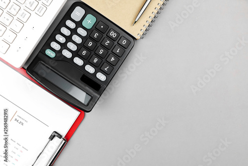 Top view of black calculator, white keyboard, financial report, and notebook on gray background with copy space. Concept of digital accounting, financial analysis, and business budget planning.