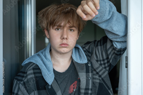 Fotografía Teenage boy standing in a doorway with hand raised above his head and a serious expression