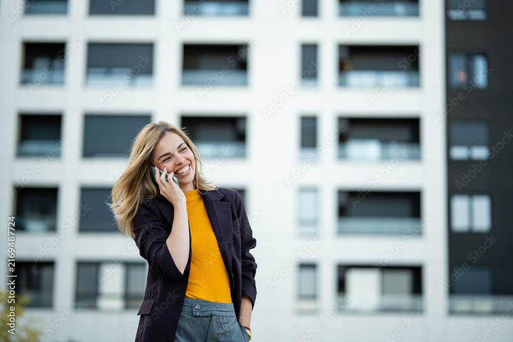 Fototapeta premium Happy young woman talking on smartphone in city