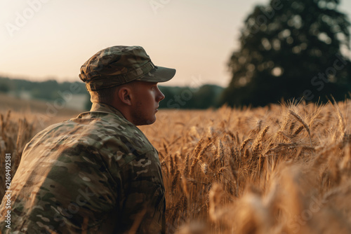 Soldier in camouflage uniform crouching low in field of golden wheat, realistic military scene. Camouflaged man observing rural landscape