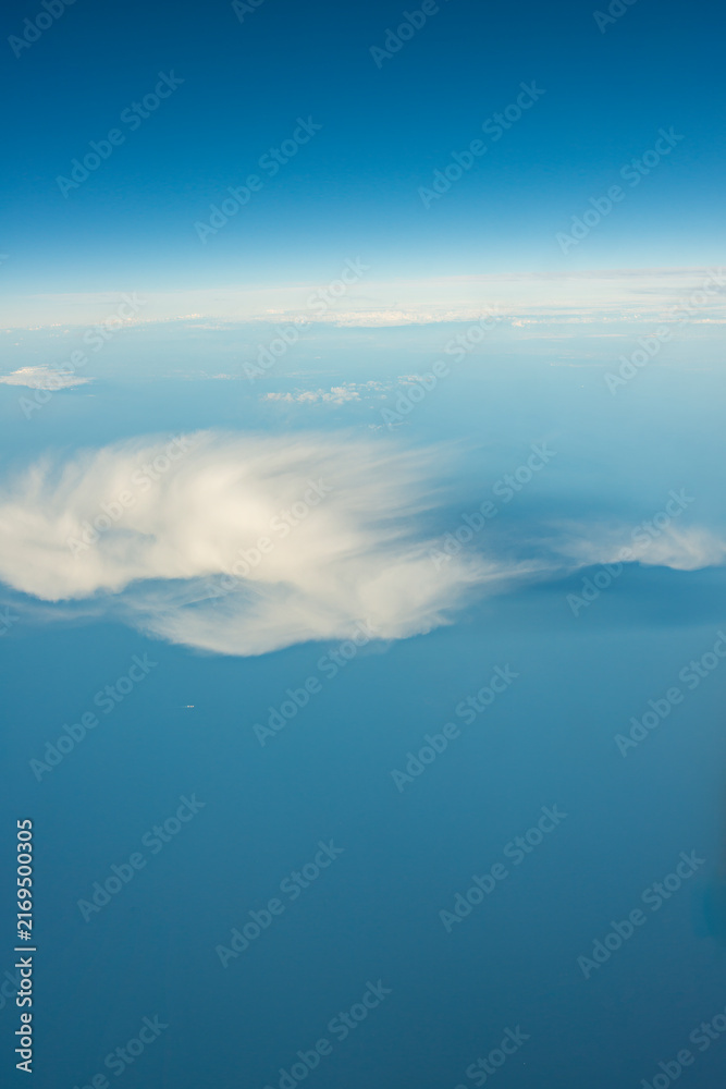 Fototapeta premium Wispy Feathered Cloud Drifting Alone Over a Calm Sea and Pale Blue Sky