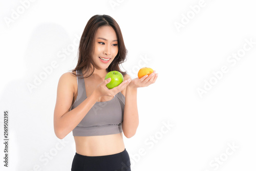 Konstfotografi Smiling beautiful asian woman in gray sportswear hold a green apple and fresh orange embodying healthy lifestyle fitness and good nutrition at studio shot on white background