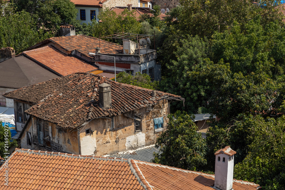 Fototapeta premium Old dilapidated historic houses with weathered tiled roofs and rustic walls hidden in greenery in Kaleici old town of Antalya, Turkey. Heritage architecture view.