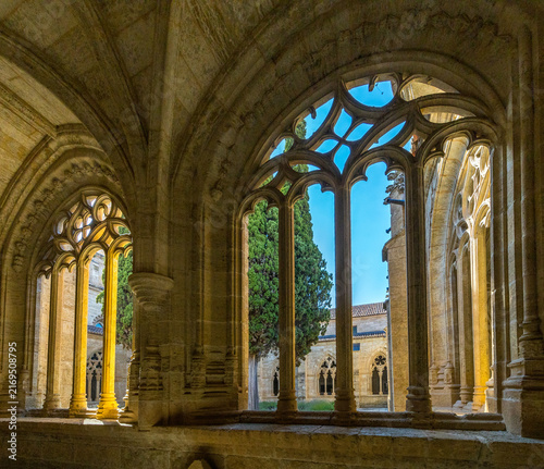 Canvastavla An ornate gothic stone tracery window frames a sunlit medieval cloister courtyar