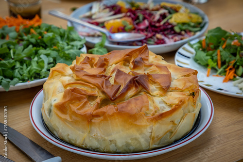 A filo pastry pie ready to be eaten, with defocused salads behind