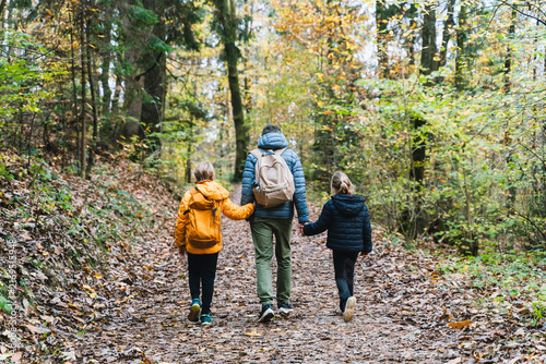 A loving family holding hands walks away down a beautiful forest path completely covered in fallen autumn leaves. 
