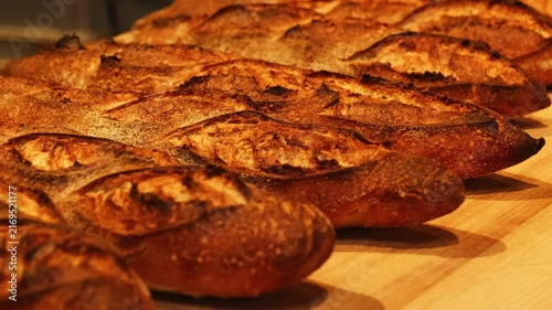 Delicious baguettes with crispy crust rest on wooden table in kitchen. Healthy fresh buns arranged on tray in craft bakery. Small business