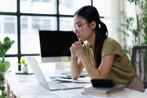 Fotografie Asian woman thinking while working on laptop