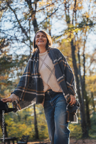 Happy mid-adult woman holding a hat in hands with a joyful smile in autumn forest.
