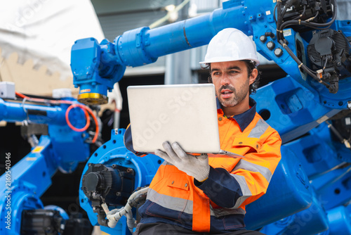 Cuadro en lienzo Robotics engineer using laptop to program industrial robot arm, automation engin