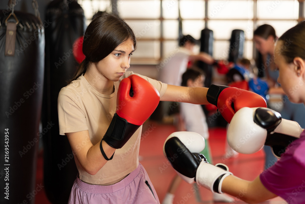 Fototapeta premium Teenage girls in boxing gloves practice punches during boxing training. Children practice self-defense techniques in the gym
