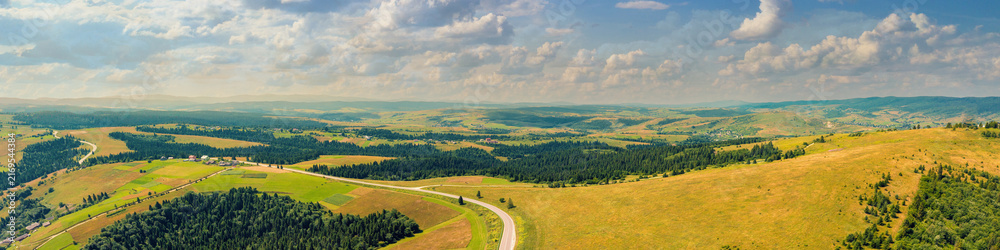 Fototapeta premium Panoramic aerial view of the countryside, country road, and cultivated and uncultivated fields in the hills