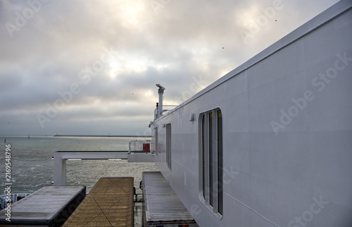 Canvastavla White superstructure and radar mast of a passenger and cargo ferry with parked freight trucks on deck, sailing out of a maritime port on a cloudy day