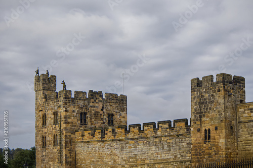Foto Majestic medieval stone castle fortress featuring ancient defense walls, battlements, and tall towers surrounded by green grass under a cloudy sky