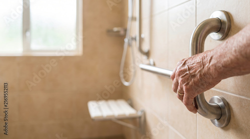 Hand holding metal grab rail in bathroom with shower seat and safety bars for elderly or disabled support