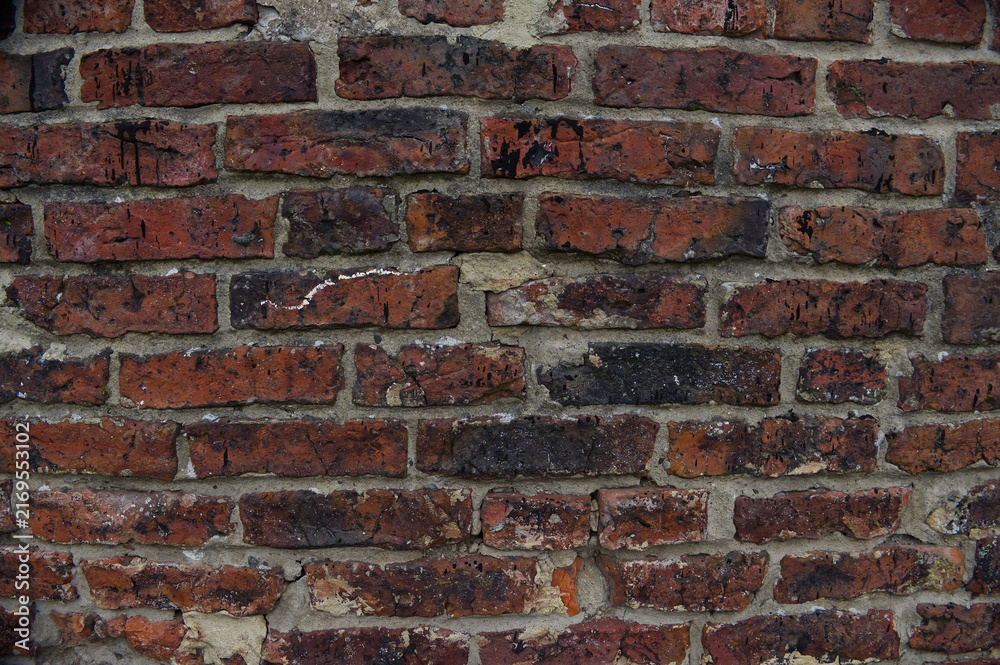 Fototapeta premium Old red weathered brick wall texture with dark grunge spots and crumbling mortar. Rustic industrial architecture background pattern.