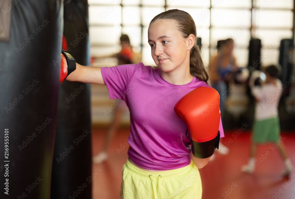 Obraz premium Teenage girl in red boxing gloves at training in the gym. Portrait of a boxing teenager. Muay Thai training for children