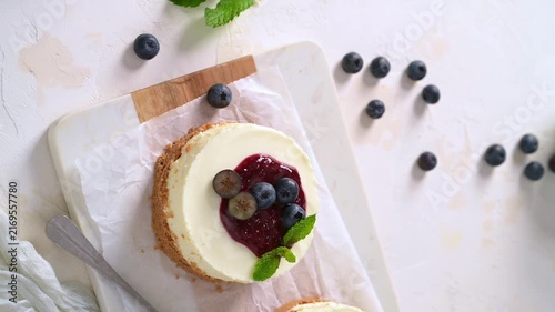 Delicious mini cheesecake topped with rich berry compote, fresh blueberries, and mint leaves on a white background.