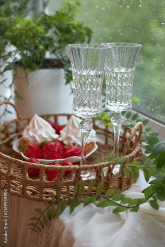 Fotografía Two crystal glasses sit on a woven tray with strawberries and meringue beside them