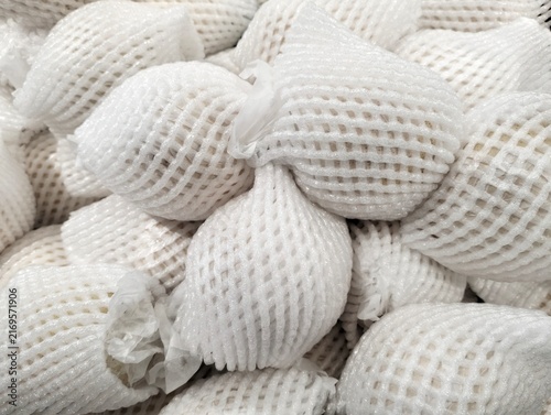 Close-up of fresh fruits wrapped in white protective foam mesh netting on display at a retail store, ideal concept for fresh produce packaging