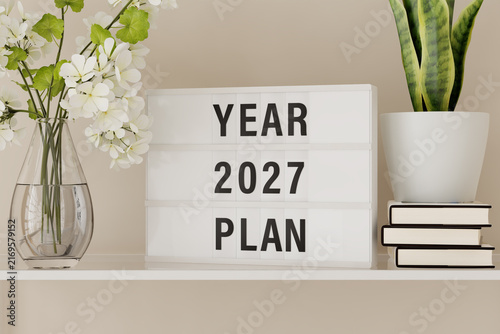 Foto A lightbox displaying the words Year 2027 Plan on a shelf with books and plants