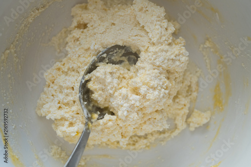 Mixing cottage cheese dough with spoon in white bowl for baking recipe concept
