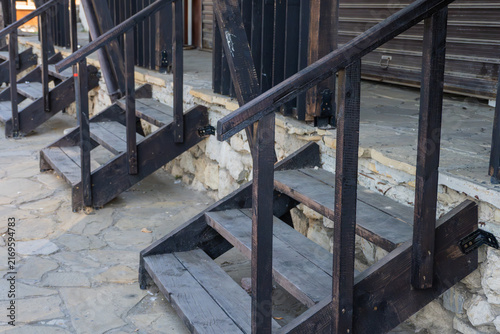 Fotografía A row of identical dark wooden staircases with simple handrails leading up to a raised stone platform along a textured flagstone pedestrian walkway